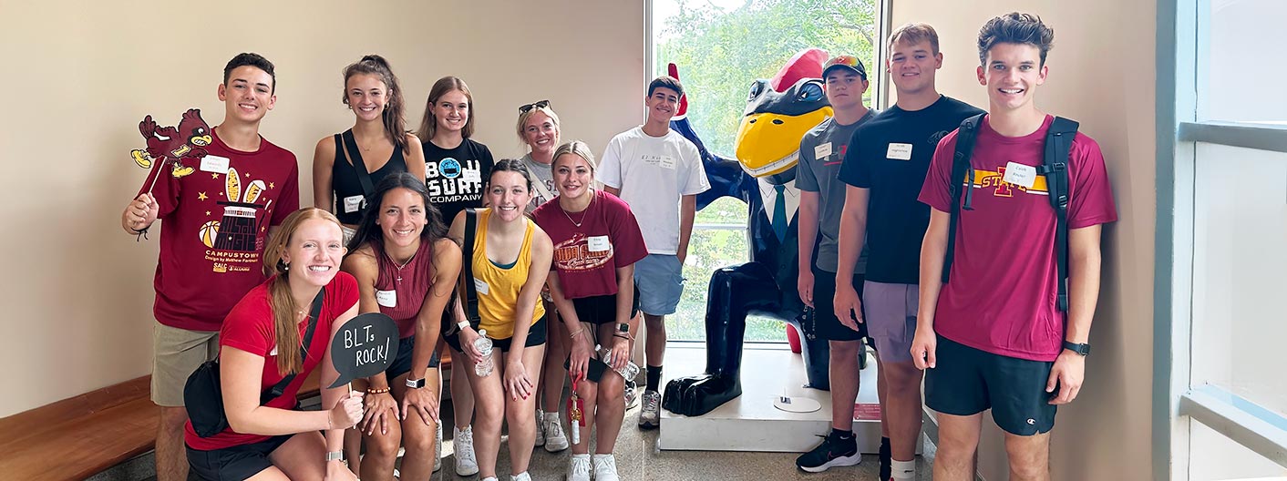 A group of students involved with Business Learning Teams (BLT) pose for the camera with Business Cy mascot.